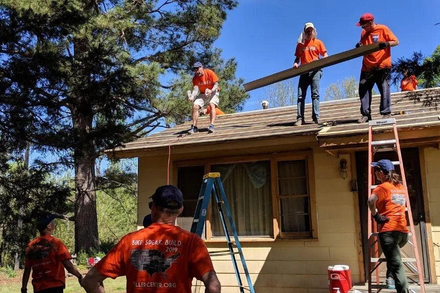 Group of volunteers replacing shingles on a roof under a blue sky