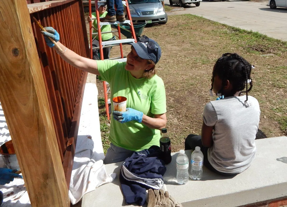 Child painting a front porch railing with help from adult