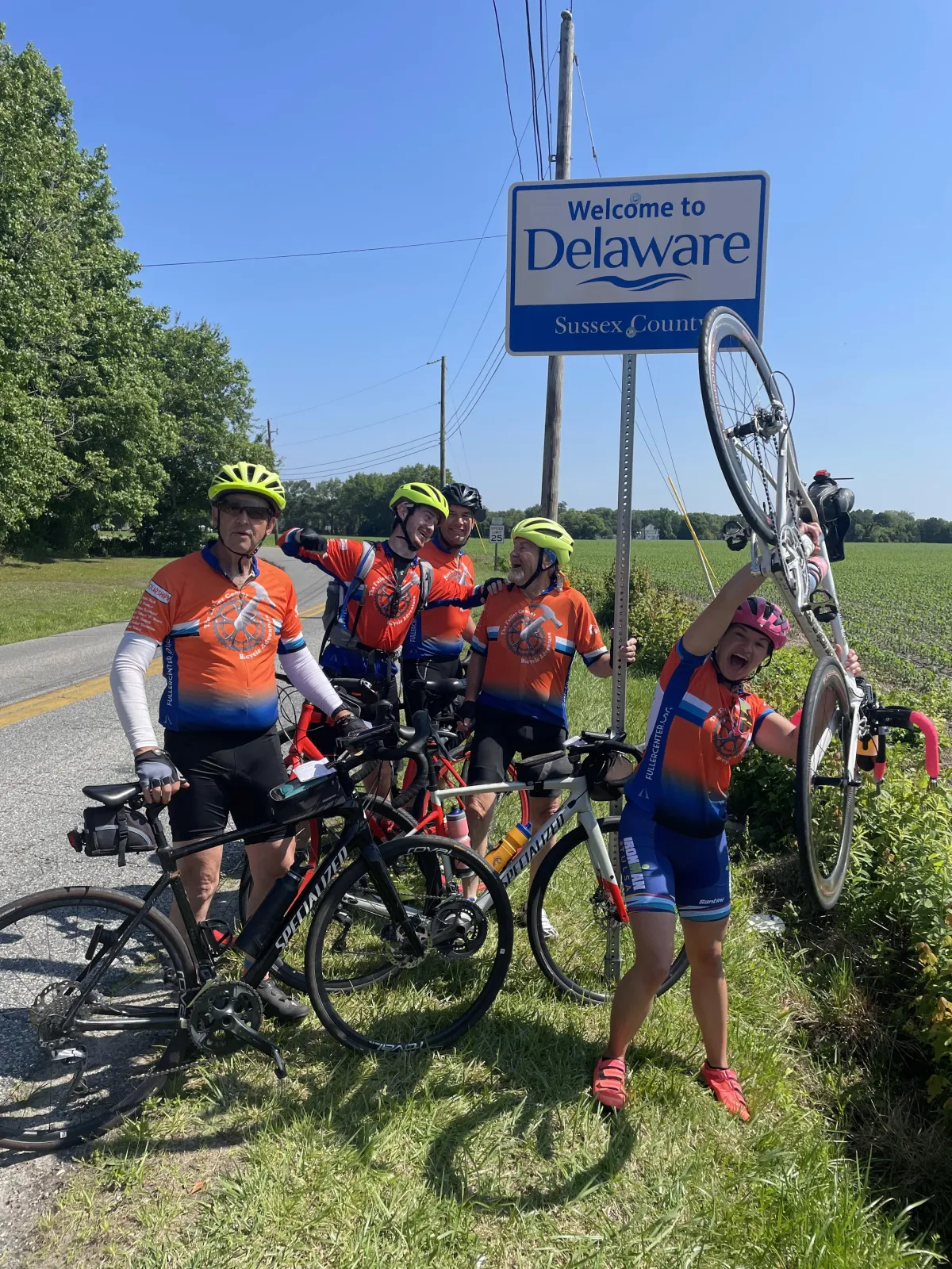 Group of 5 cyclists celebrating under Delaware sign