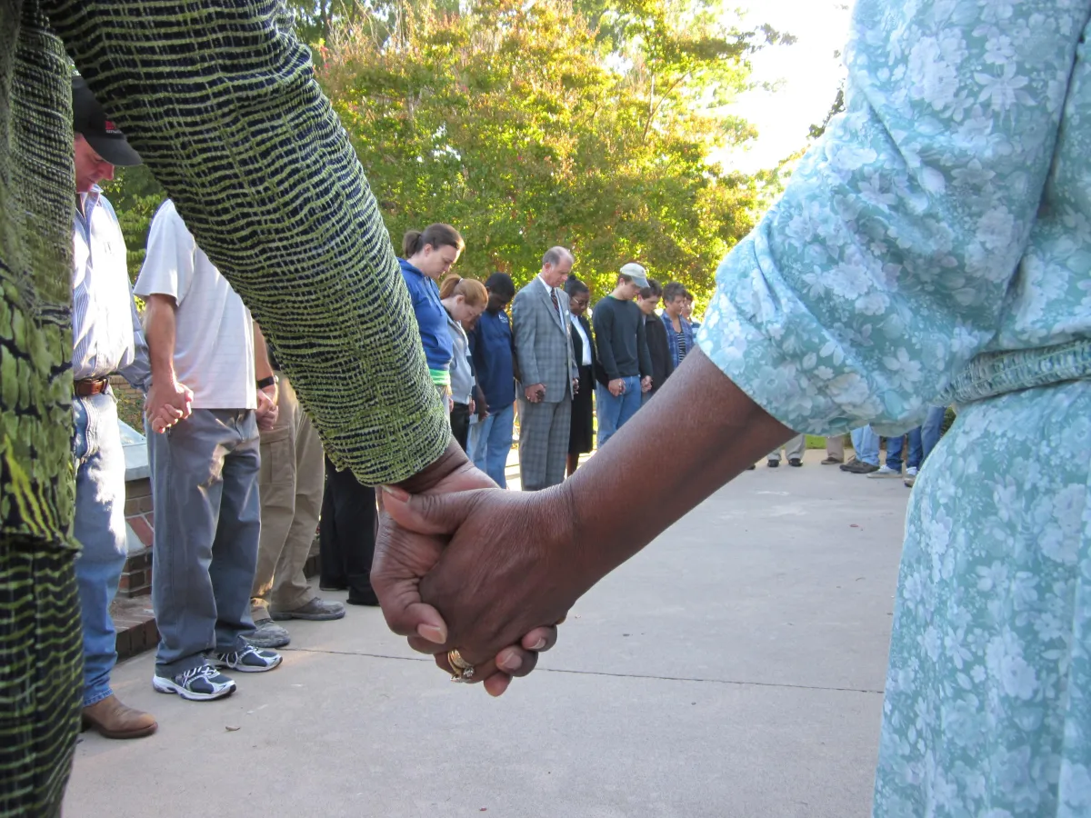 Volunteers holding hands in a prayer circle before beginning a home repair effort, reflecting the faith-centered mission.