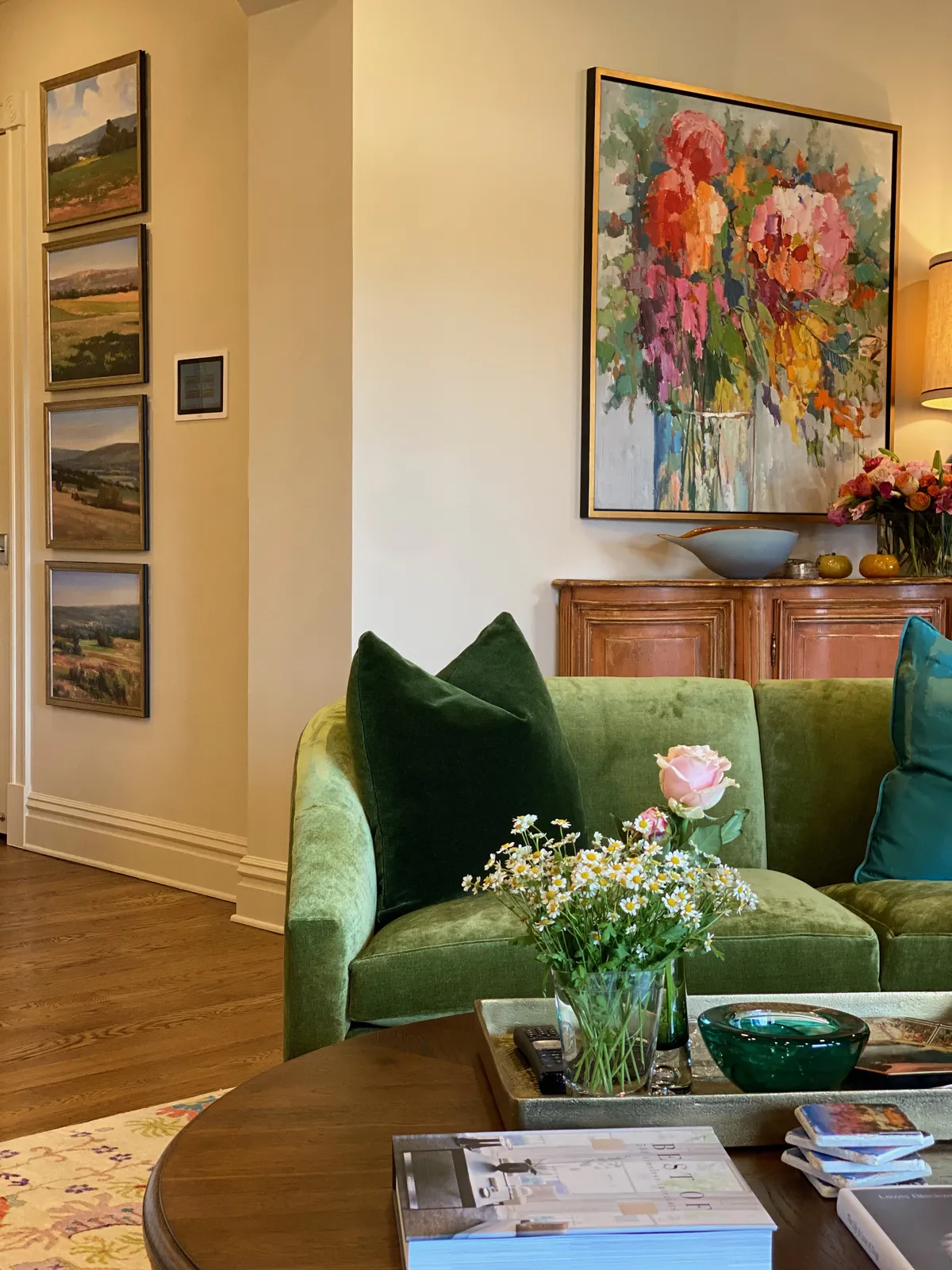 Green velvet sectional sofa with floral artwork above a wood credenza