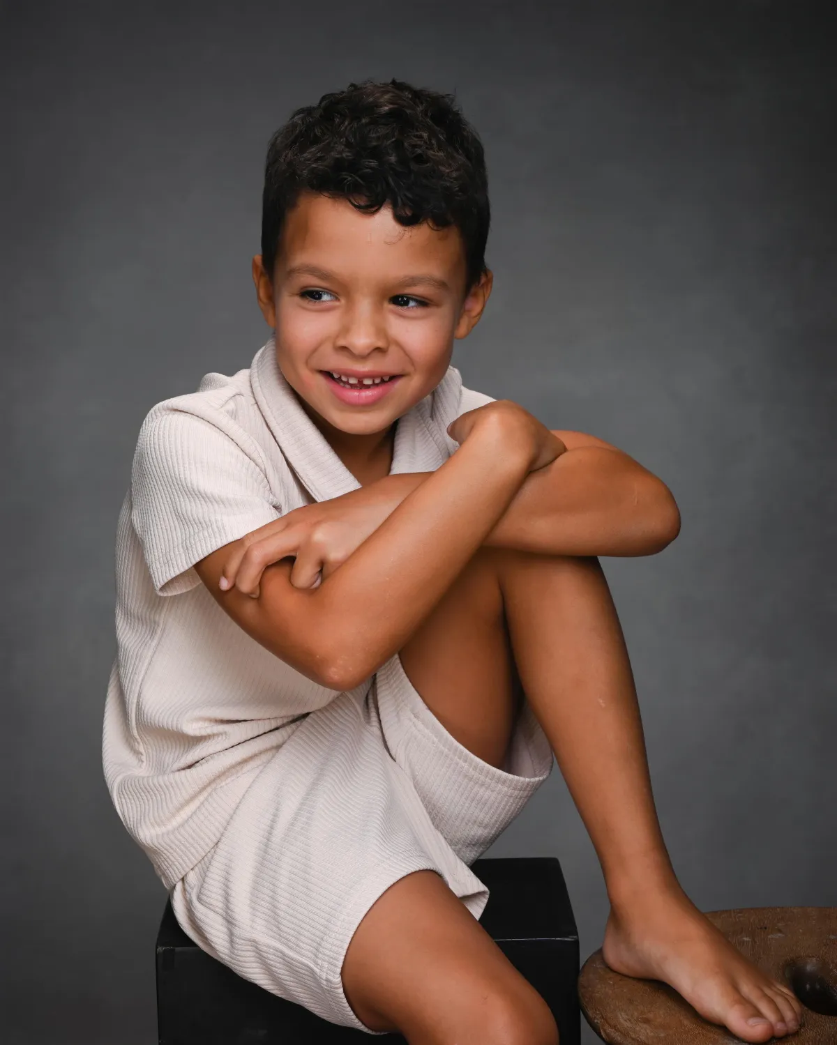 Studio headshot of a young boy laughing softly, gazing to the side with natural, joyful expression.