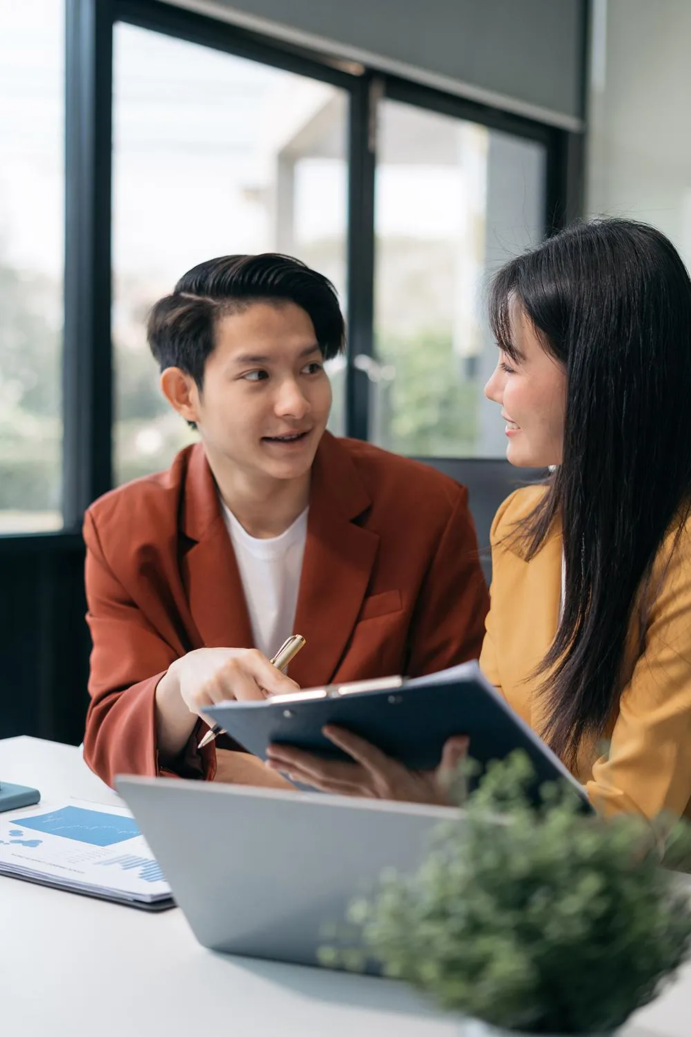 Two Asian business professionals collaborate at a table, focused on a laptop during a meeting