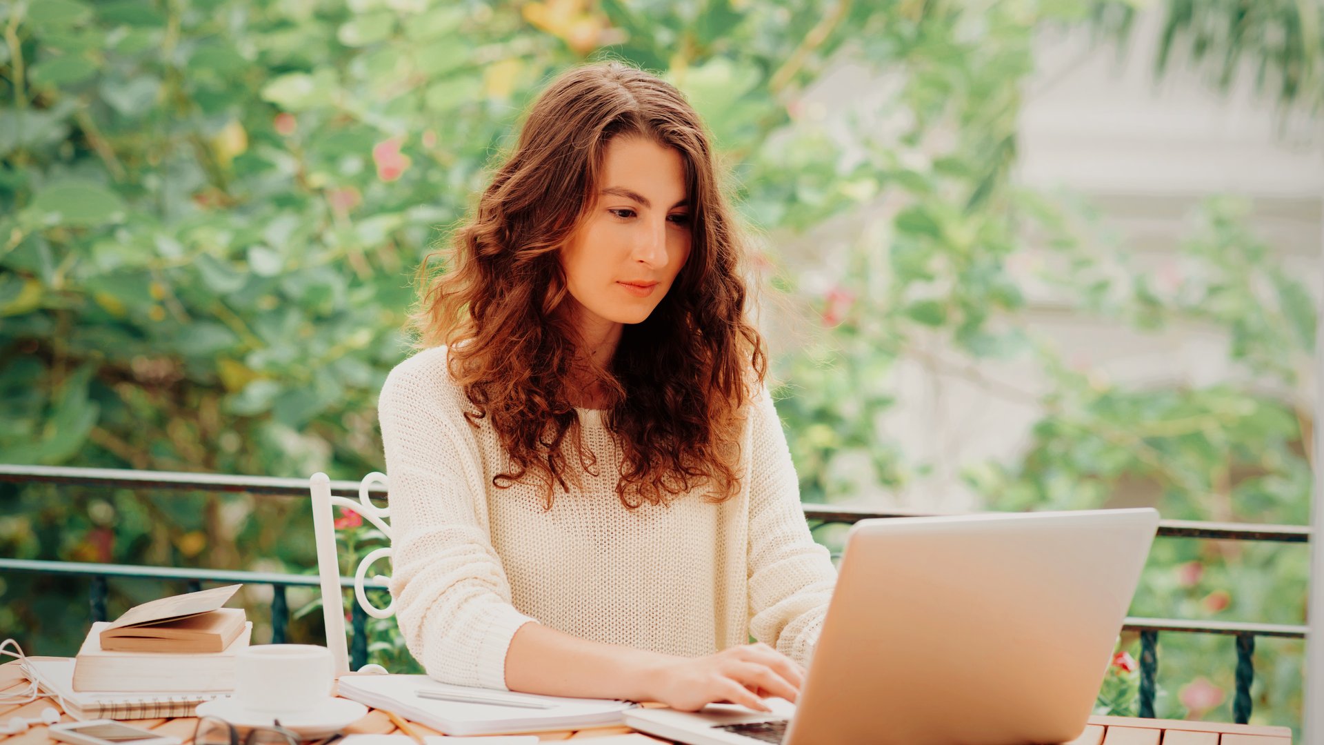 Coach and content creator working from an outdoor cafe, researching Kajabi alternatives for her business.