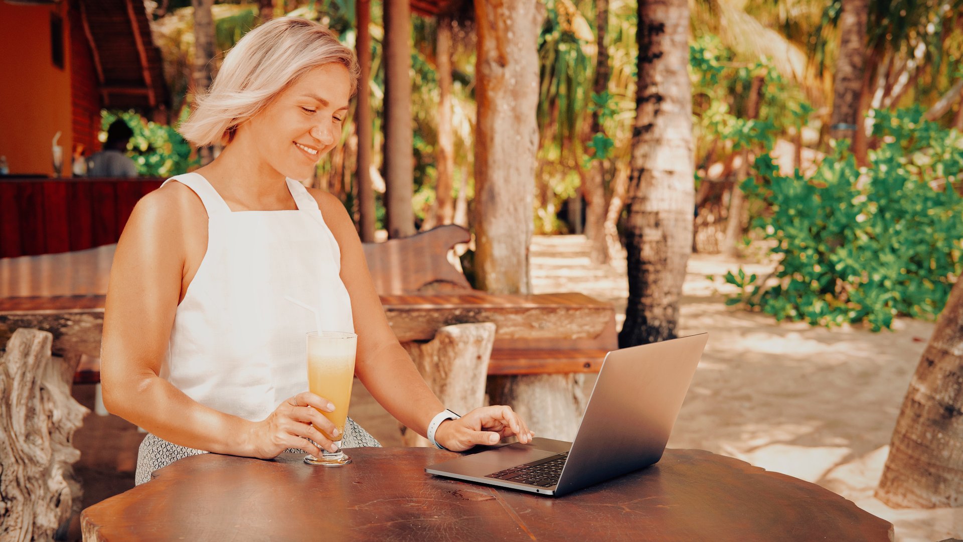 Woman relaxing with a tropical drink beside her laptop, having reclaimed her time by putting AI to work in her business.