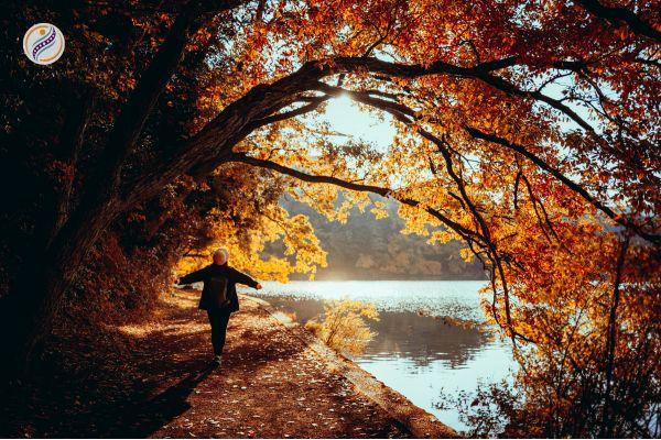 Person walking with arms open under golden autumn trees beside a lake, Right Spot Wellness fall newsletter