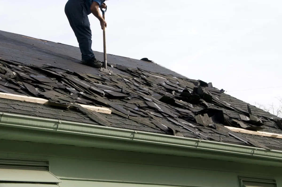 Worker repairing damaged roof with black shingles, roof repair and replacement service in DFW by ETRR Construction.