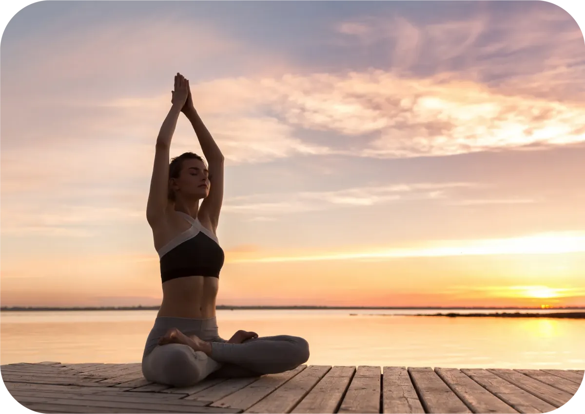 A young women does yoga on a dock at a lake at sunset