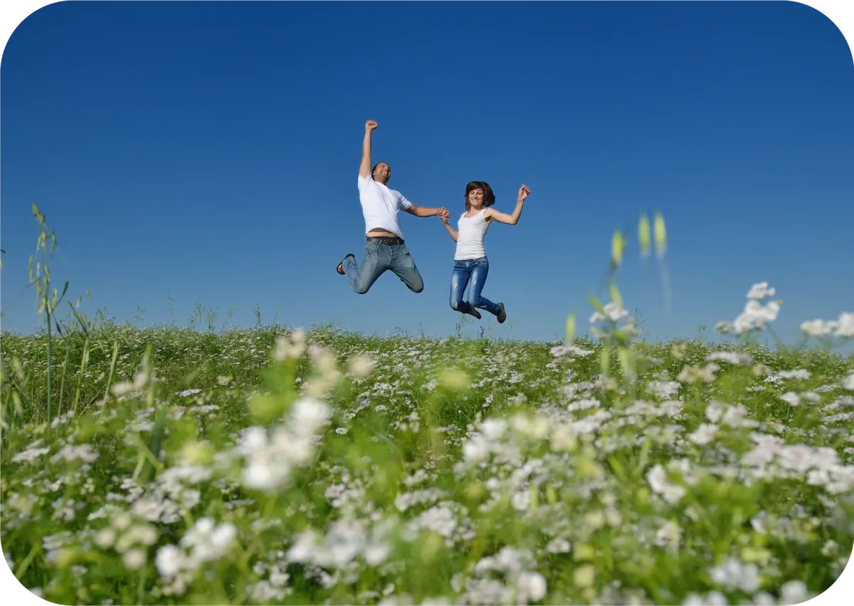 Two people in a healthy relationship jump in a field