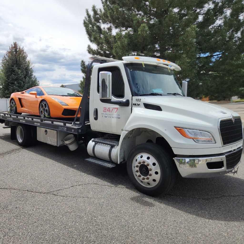 White 24/7 Towing & Recovery flatbed tow truck carrying an orange sports car