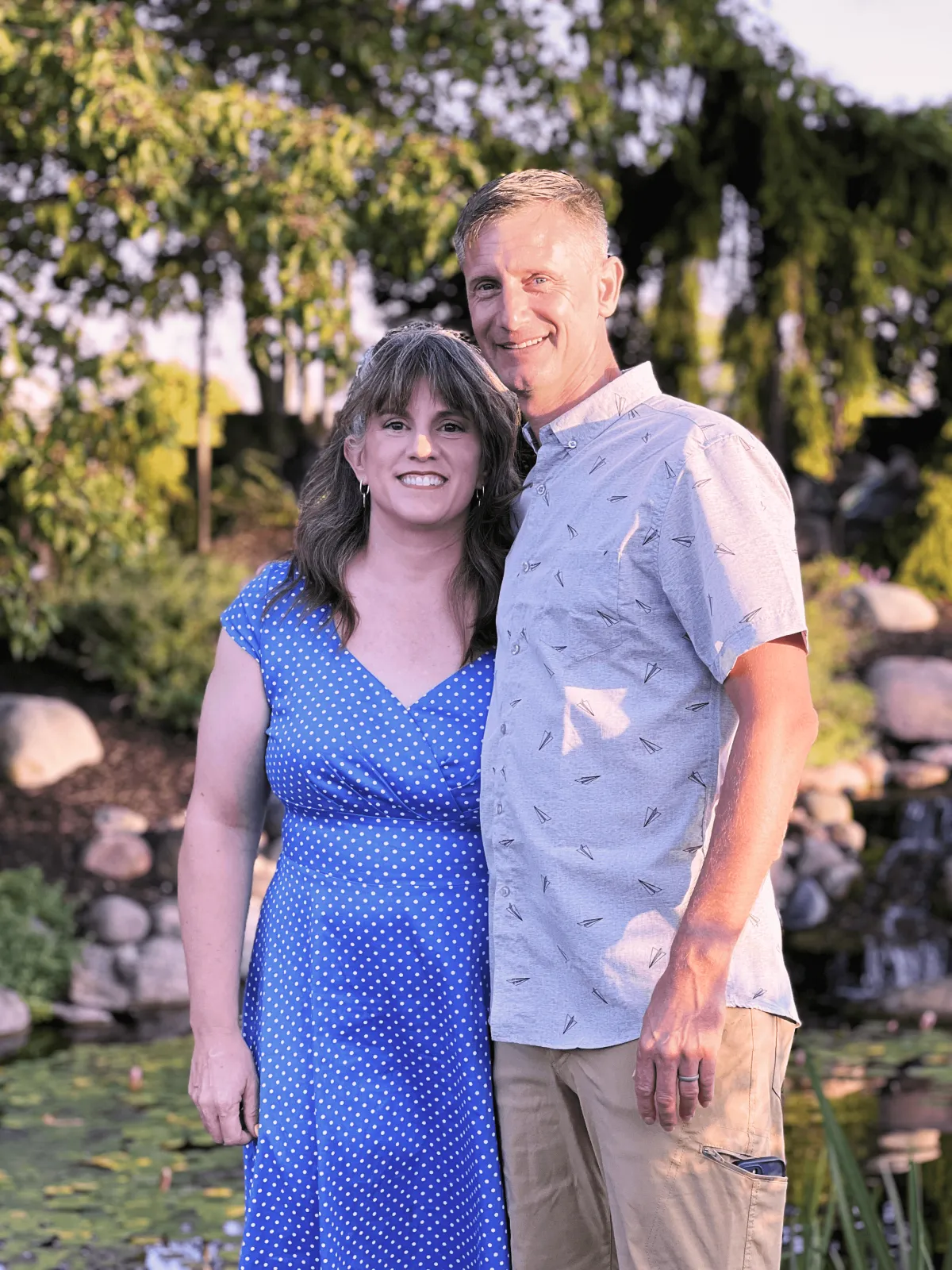 Scott and Kati Molchan, founders of LeadSpeed, standing together in a landscaped garden setting, smiling and promoting their marketing services for landscaping businesses.