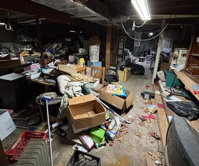 Cluttered basement filled with boxes, furniture, and household clutter before a basement cleanout service