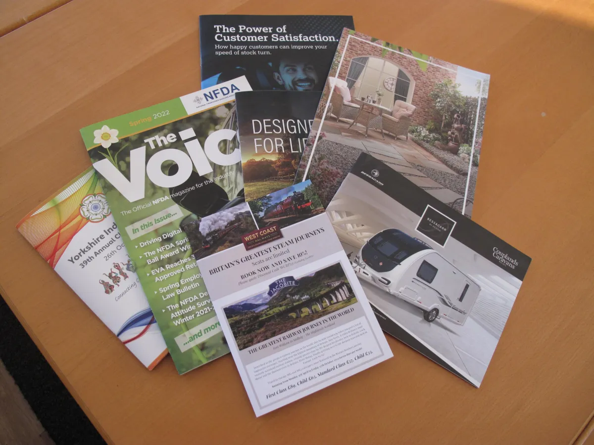 A mixture of colourful magazine's and leaflets spread out on a wooden table.