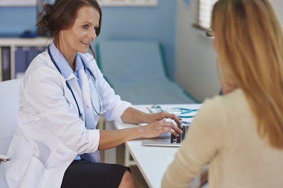 A female doctor or medical professional smiling and talking to a patient.