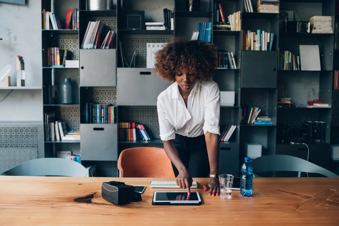 Woman leaning over a desk, focused on a tablet, symbolizing managing overwhelming tasks like marketing with digital tools