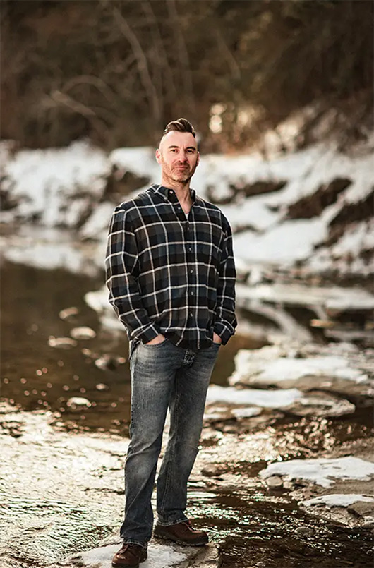 A determined, mid-40s stepdad stands at the center of a blended family in a warmly lit living room, his posture confident yet approachable. The family, diverse in age and ethnicity, gathers around him, each member engaged in a different activity, symbolizing unity through individuality. The scene is vibrant, with soft blue and teal accents reflecting hope and transformation.