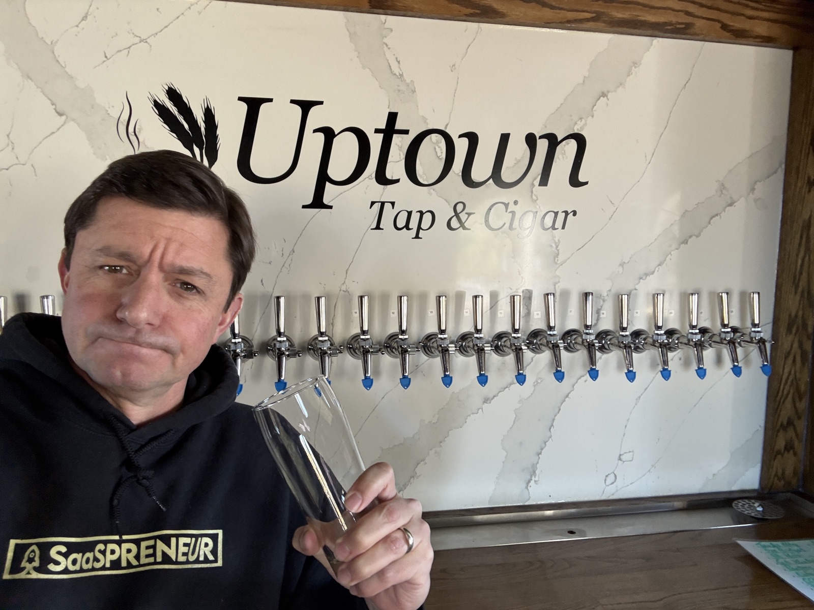 Owner Greg Walbridge standing at the 22-tap wall under the Uptown Tap & Cigar sign on St. Simons Island