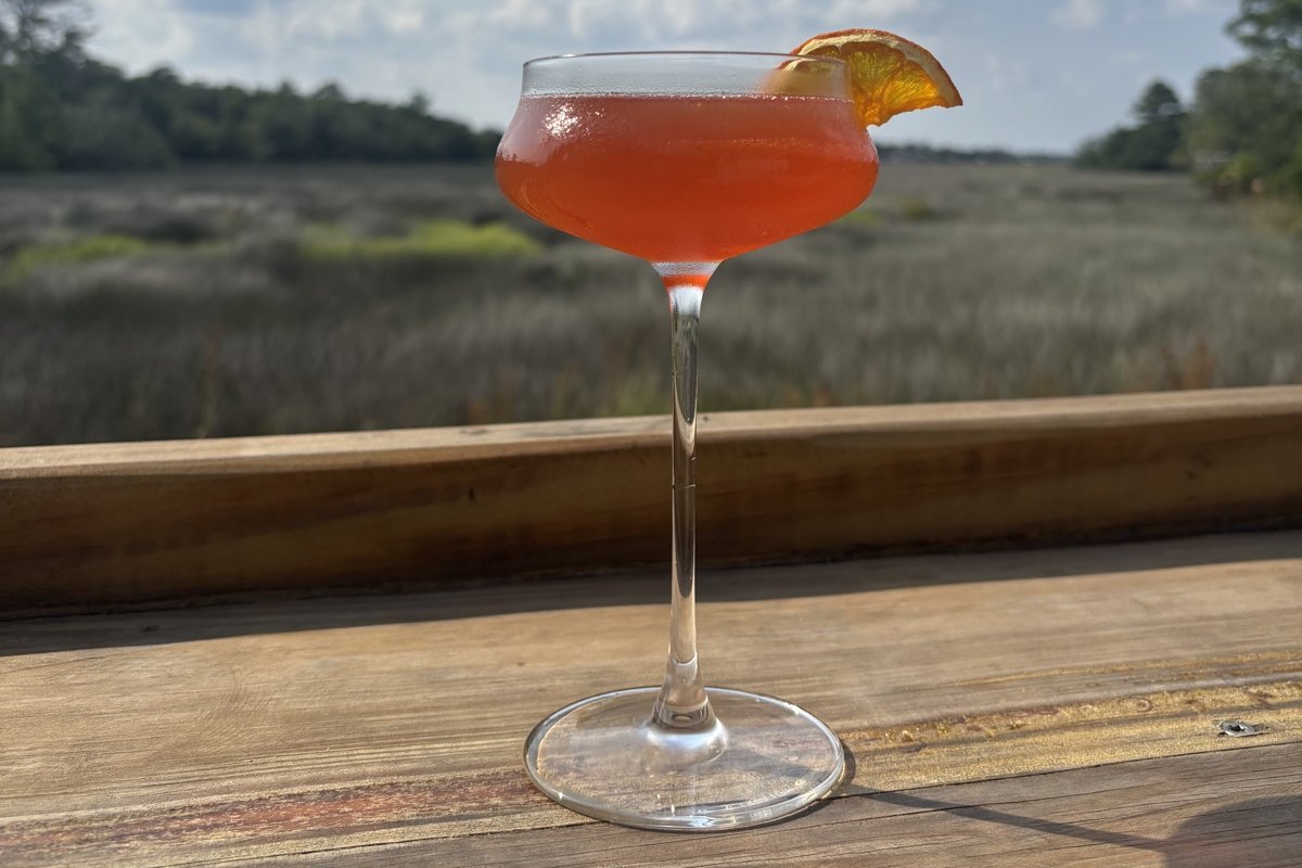 Craft cocktail with a dried orange wheel on the deck rail overlooking the St. Simons marsh