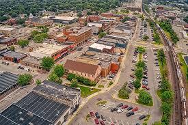 Aerial view of a downtown district with streets, shops, parking lots, and green trees lining the sidewalks.
