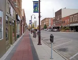 Street-level view of a downtown area with brick buildings, sidewalks, streetlights, and storefronts along a pedestrian-friendly street.