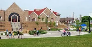A public park area in front of brick buildings with people walking and relaxing on the grass in the Czech Village or New Bohemia district.