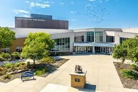 Modern building with a glass entrance and landscaped walkway in front, surrounded by greenery and blue skies.