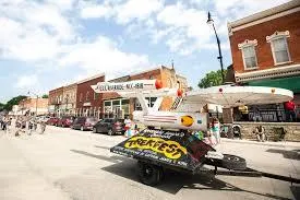Street view of a vibrant downtown area with outdoor dining, red-brick buildings, and a decorative airplane statue in the foreground.