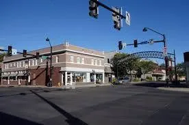 Intersection in a small downtown area with a corner brick building, traffic lights, and a clear blue sky overhead.