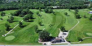 Aerial view of a lush green golf course with fairways, sand traps, and a clubhouse surrounded by trees.
