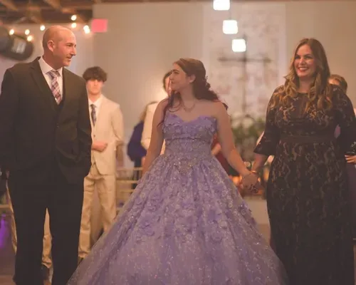A happy quinceañera family standing together inside a church, with the quinceañera in a blue gown and her relatives dressed elegantly beside her.