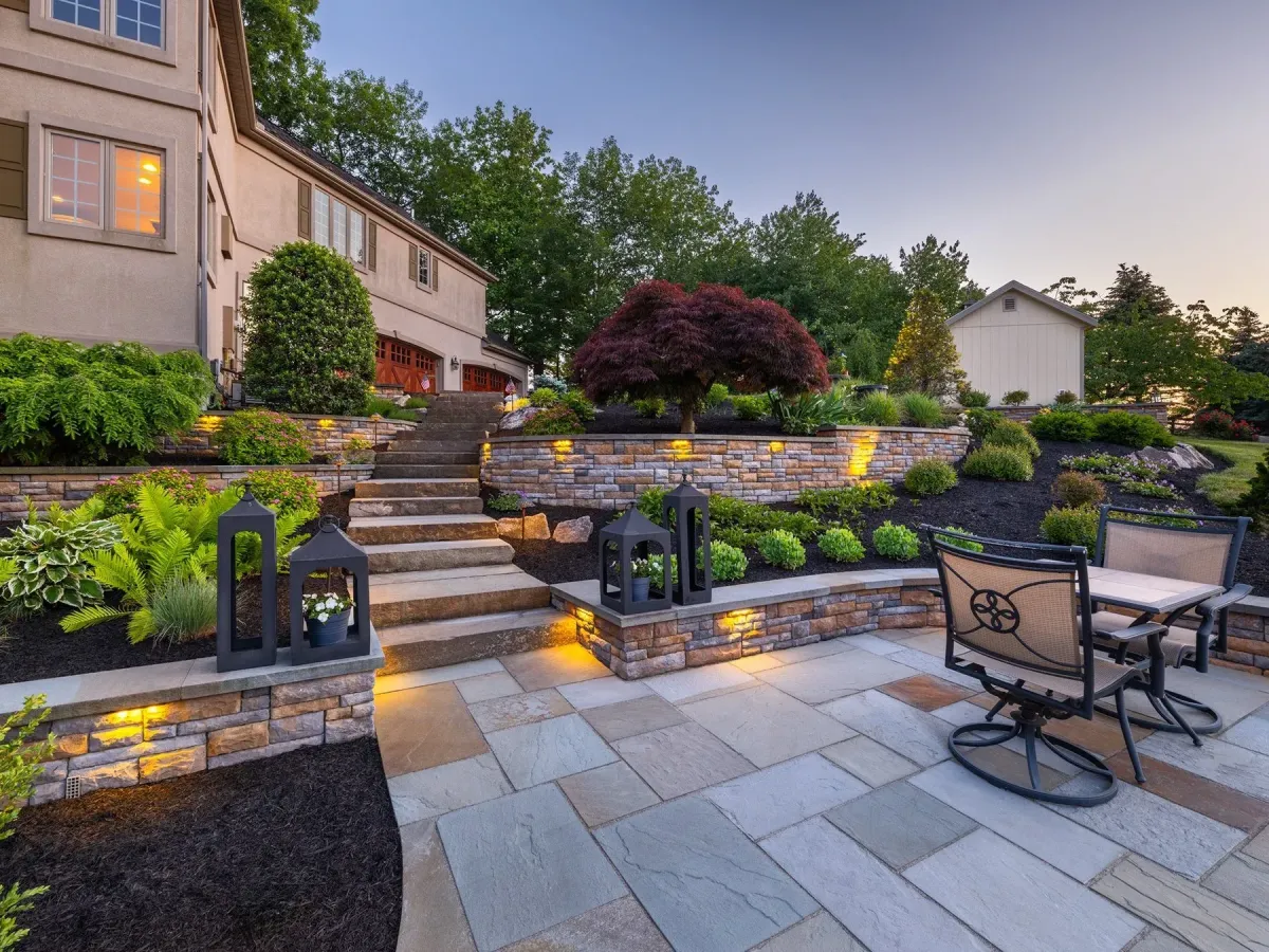 Beautiful backyard landscape with stone patio, lighting, and greenery designed by AMG Construction & Landscaping in Kearns, Utah