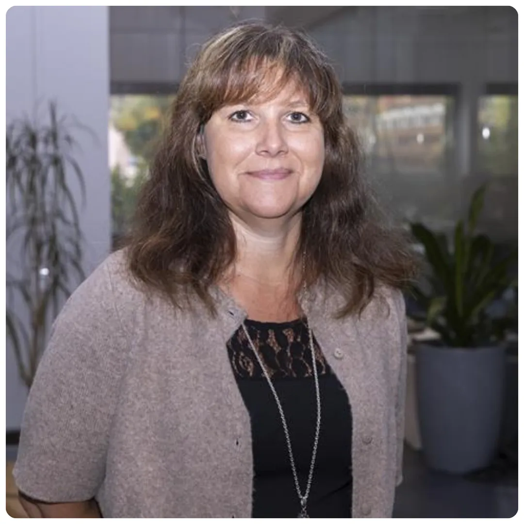 Sofia Fröberg, auktoriserad redovisningskonsult på Affärskompetens-Företagarbyrån er mot kameran. Hon har en svart t-shirt under en ljusbrun kofta, runt halsen hänger ett längre silvrigt smycke. I den något nedtonade bakgrunden syns två stora gröna växter och ett stort fönster.