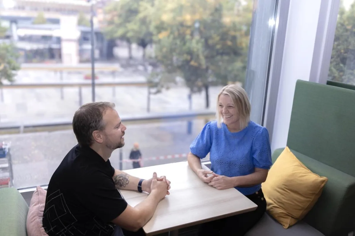Två företagsutvecklare stitter vid ett bord vid ett stort fönster med utsikt över gatan nedanför. 
