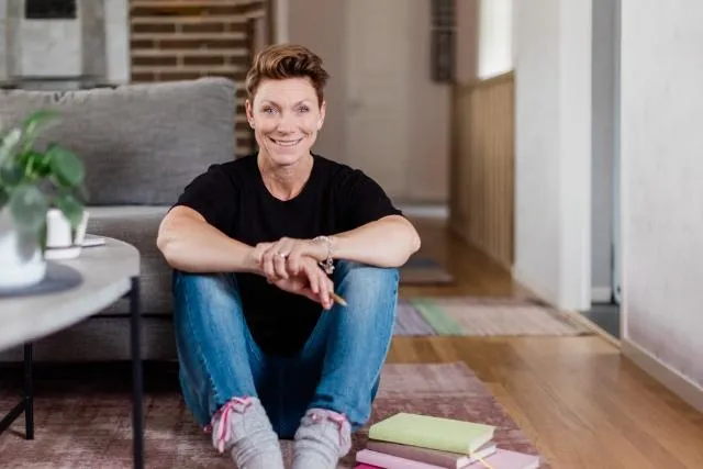 Jill Nyqvist påSolopreneurerna och Företagarbyrån sitter på golvet bredvid ett runt soffbord och en grå soffa. På golvet bredvid henne ligger tre anteckningsböcker. Jill sitter framåtlutad och vilar sina armar mot sina knän.