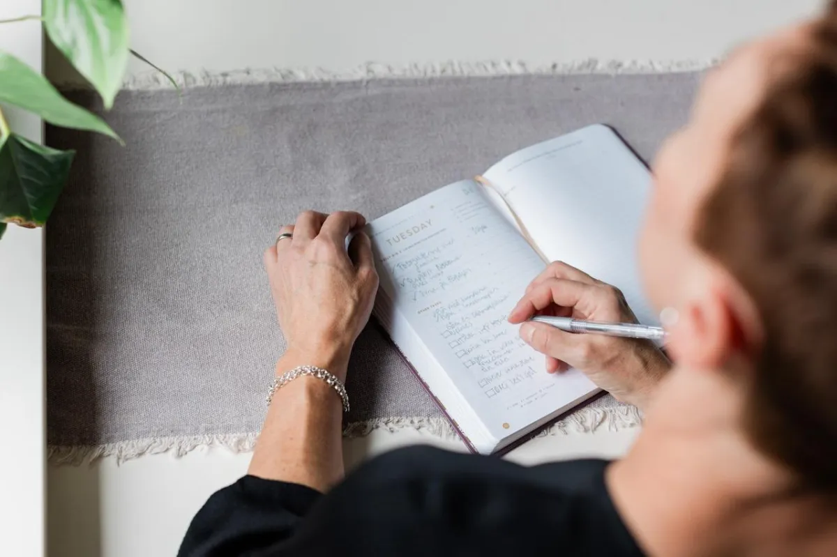 en kvinna man ser ovanfrån skriver i ett antckningsblock.