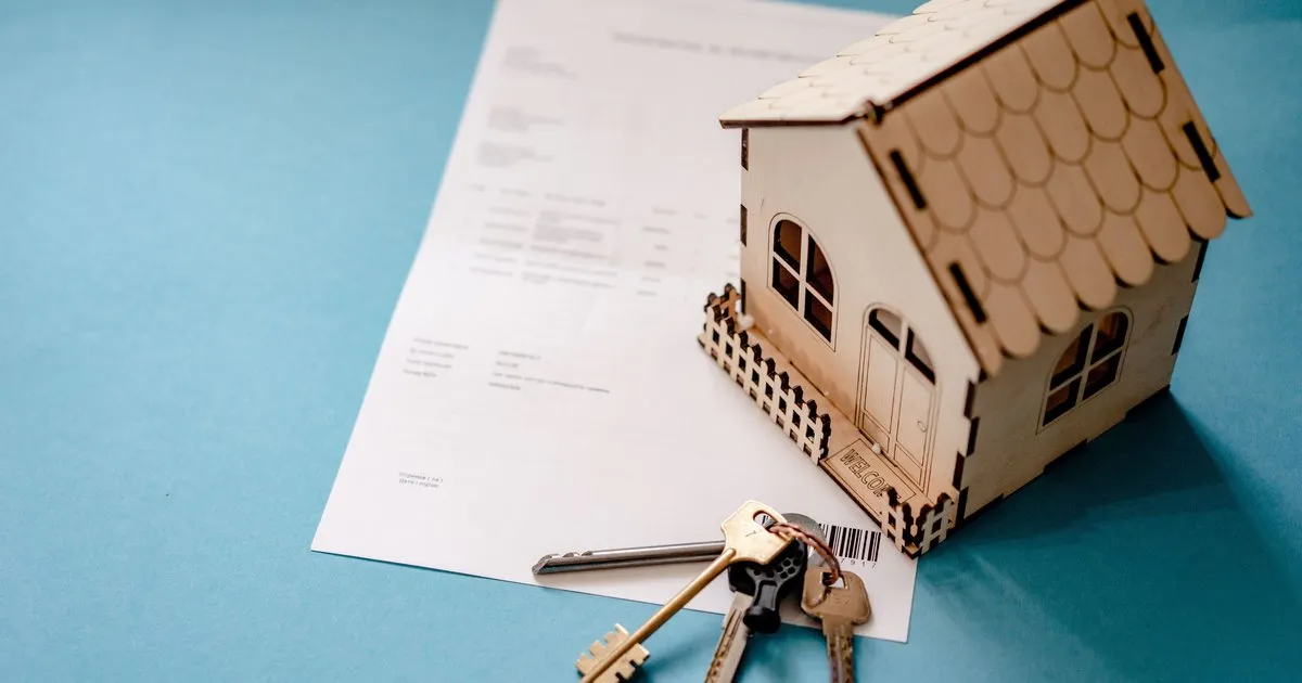Miniature wooden house model with a set of keys resting on a document