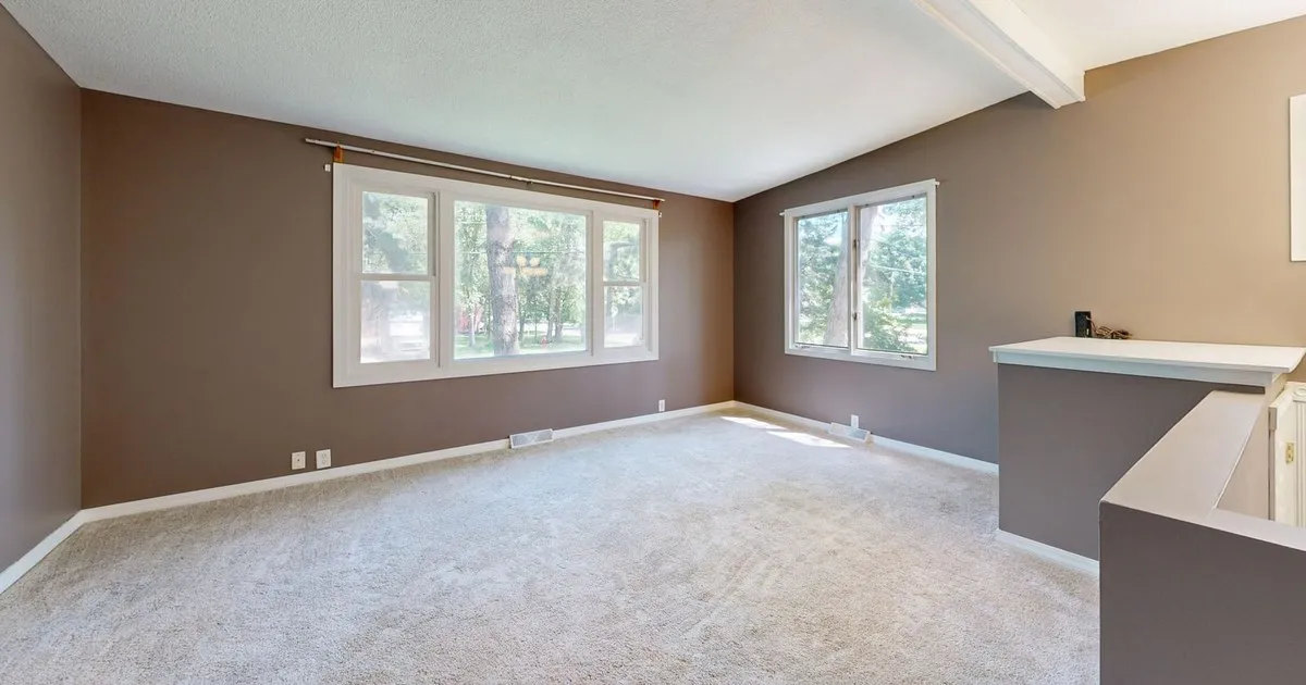 Empty carpeted living room with large windows and natural light