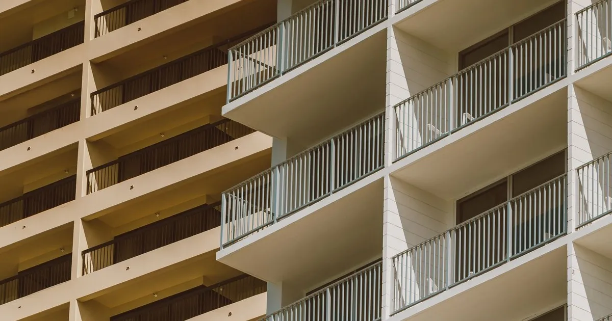 Rows of balconies with white railings on a beige condominium building in sunlight
