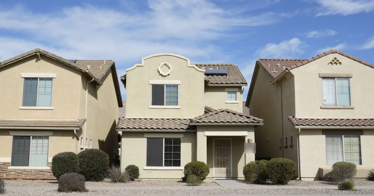Three two-story stucco homes with tile roofs and desert landscaping under a blue sky