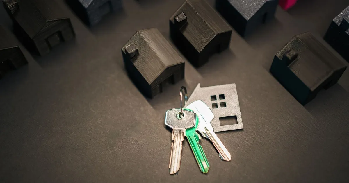 A set of house keys lying beside small dark model houses on a gray surface