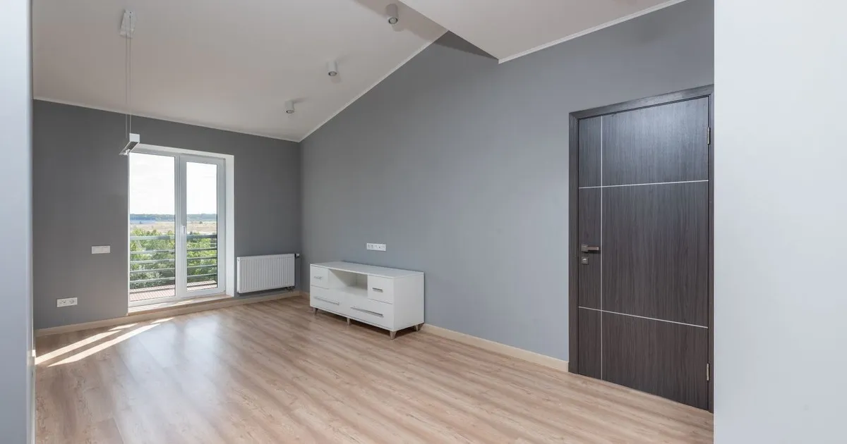 Empty gray room with light wood floor, a white low cabinet, and a glass balcony door
