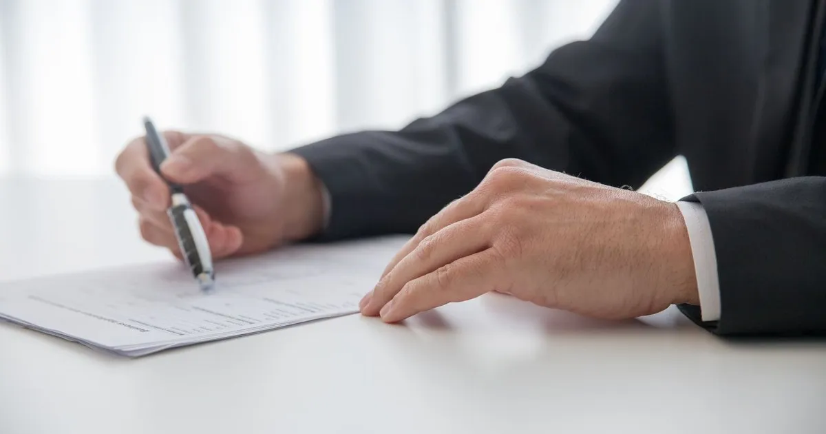 Hands holding a pen over a paper document on a white desk