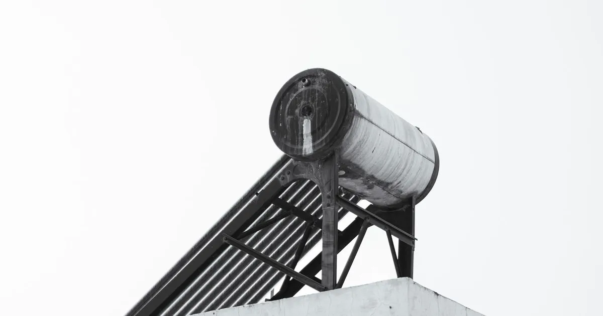 A cylindrical solar water heater tank on a rooftop against a pale sky