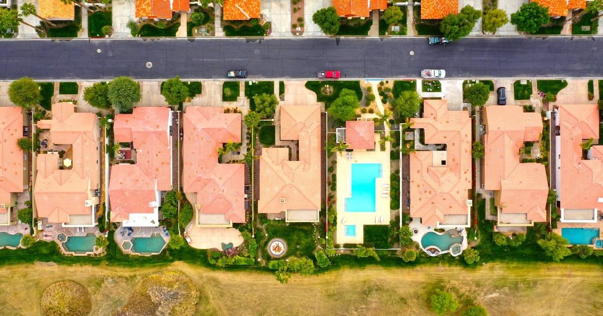 Aerial view of a planned neighborhood with tile-roof homes, backyard pools, and a shared community pool