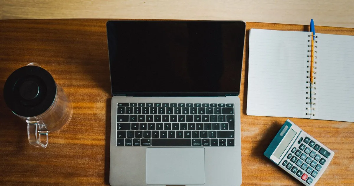 Overhead view of a laptop, notebook, and calculator on a wooden desk