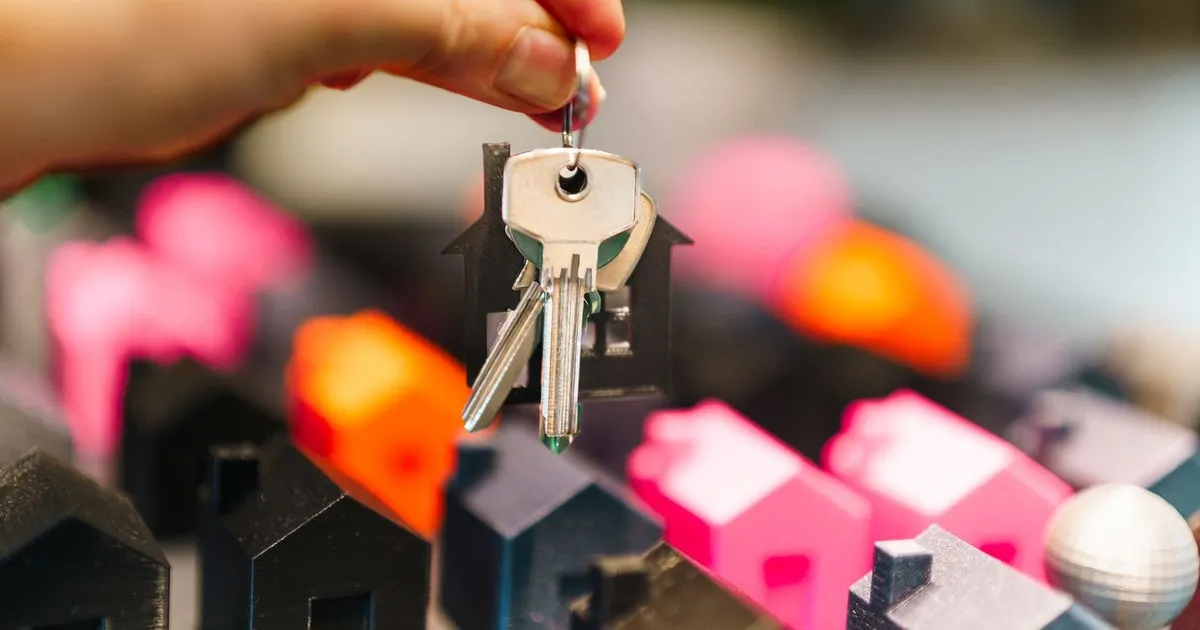 Hand holding house keys above small model houses