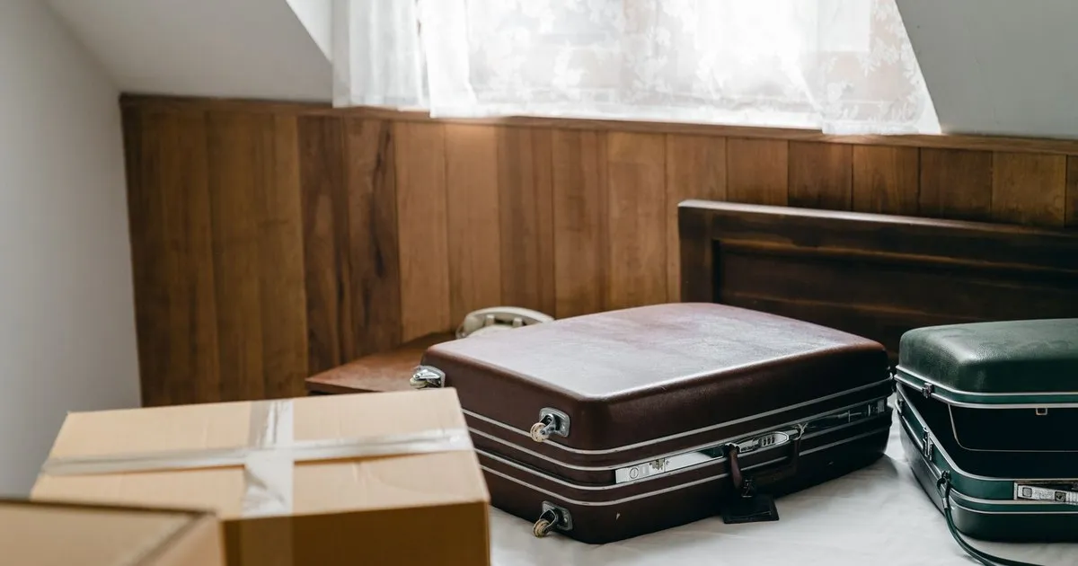 Two suitcases and a taped moving box on a bed in a bright room