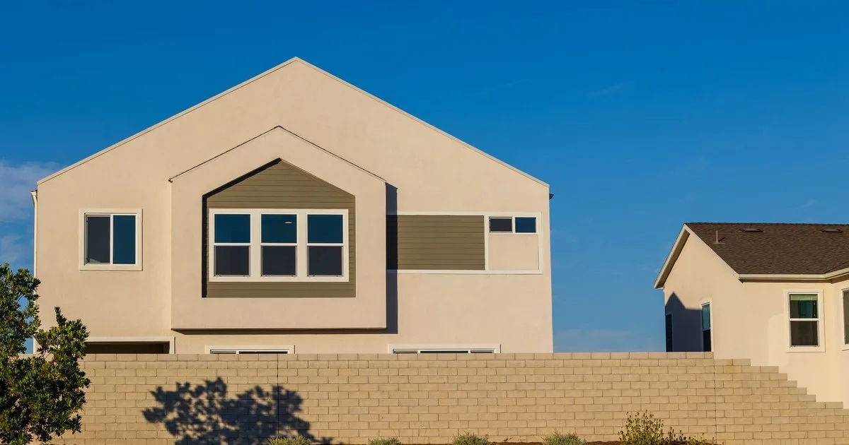 Two-story stucco home behind a block wall with desert landscaping under a clear blue sky