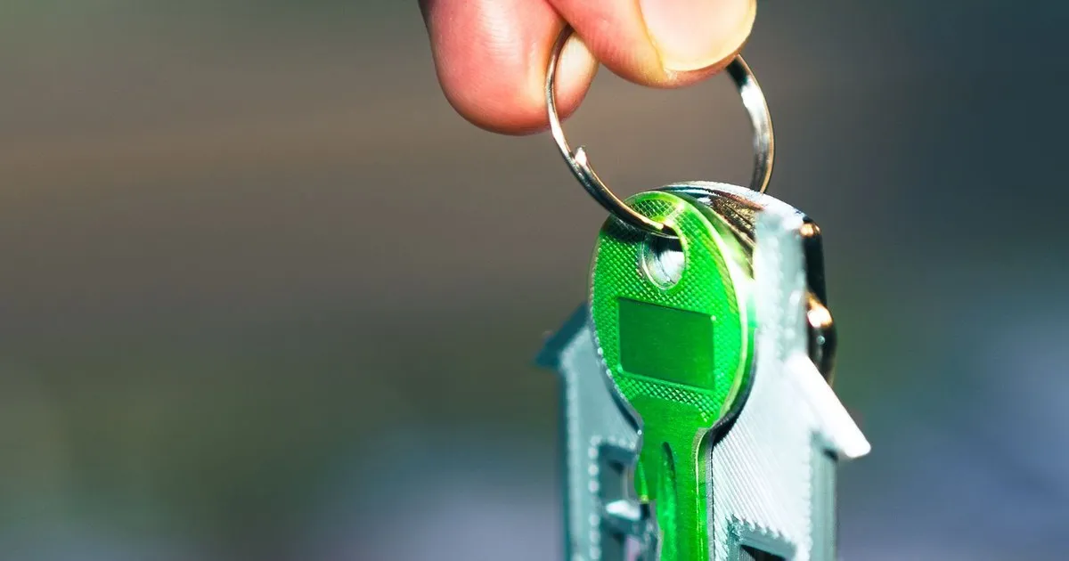 A hand holding a house key on a house-shaped keychain