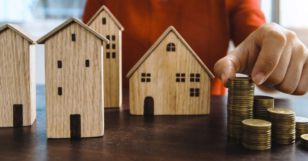 Small wooden model houses on a table next to stacks of coins